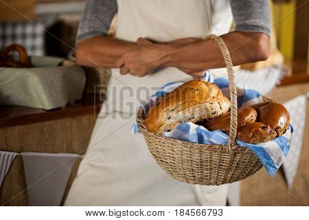 Mid-section of female staff holding wicker basket of breads at counter in bakery shop