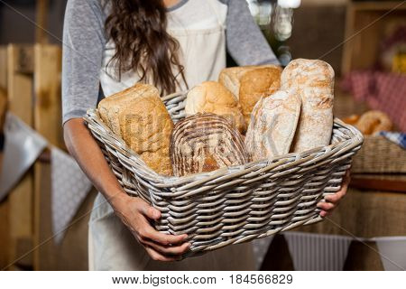 Mid-section of female staff holding wicker basket of various breads at counter in bakery shop