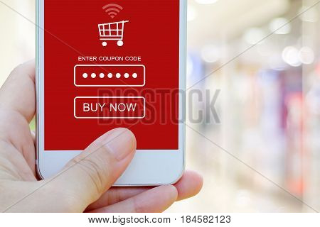 Hand holding smart phone with discount coupon code on screen over blur store background on line shopping business E-commerce technology and digital marketing background