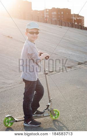 Little Boy In Sunglasses And A Cap Riding A Scooter,