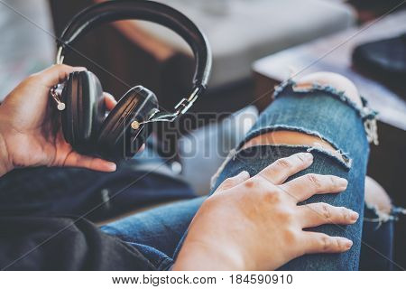 A woman wearing ripped jean holding headphone and sitting in modern cafe with feeling relax