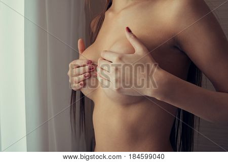 The girl covers her bare chest with her hands.