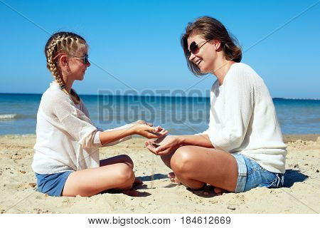 Daughter and her mom playing with sand on the beach