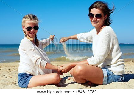 Daughter and her mom playing with sand on the beach