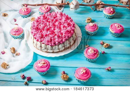 Cake and cupcakes with pink cream on blue wood background. Pink cakes