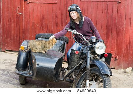 Photo of girl on vintage motorbike in pilot cap with cat