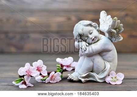 Angel guardian sleeping and spring flowers on wooden background