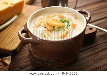Delicious beer cheese soup with croutons and onions on table