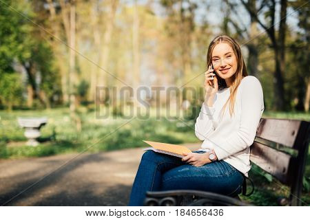 Portrait Of Attractive Young Professional Woman Using A Smartphone While Sitting On A Wooden Bench I