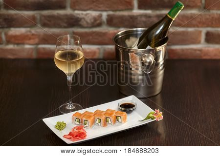 Philadelphia maki sushi rolls with salmon cheese cream cucumber on white plate and glass of wine