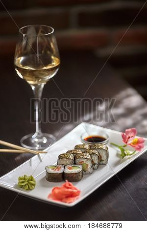 Sushi rolls with salmon and nori on white plate and glass of wine vertical photo