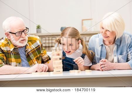 Happy Grandparents With Granddaughter Playing Jenga Game Together At Home