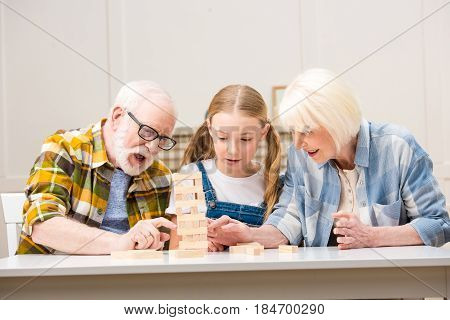 Emotional Senior Couple With Granddaughter Playing Jenga Game At Home