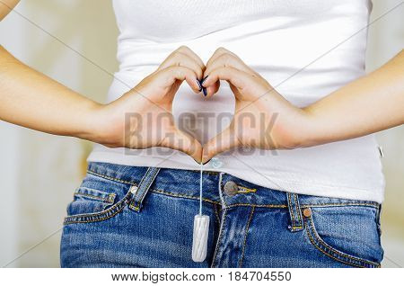 Young sexy beautiful woman holding a menstruation cotton tampon with both hands and doing a heart sign with her hands pointing in front of her jean.