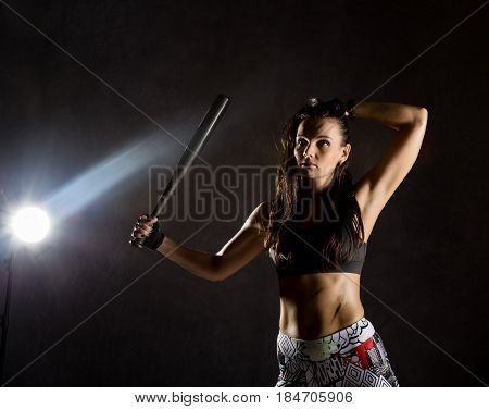sexy athletic woman with baseball bat on dark background in the beam of a searchlight.