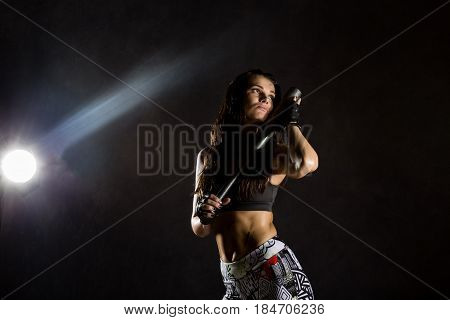 sexy athletic woman with baseball bat on dark background in the beam of a searchlight.