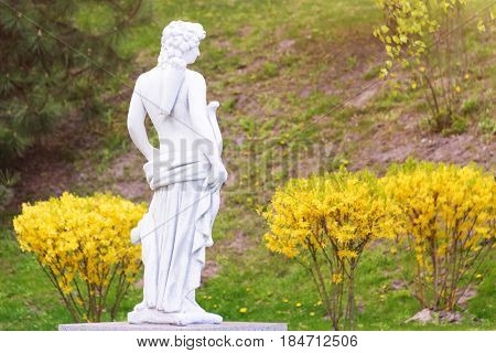 Sculpture in classic style. Statue of a man hunter with bow in the park.