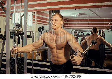 Young strong athlete with a beautiful naked torso doing muscle exercises in the gym