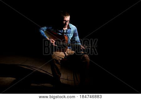 Young Musician In Plaid Shirt Playing The Guitar And Singing On Dark Background