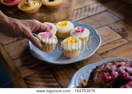 Cropped image of senior woman holding cupcake at table in cafe shop