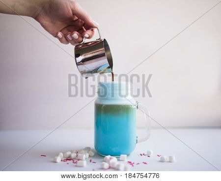 Woman is pouring coffee in cup of colored blue milk. Milk shake cocktaill frappuccino. Unicorn coffee unicorn food.