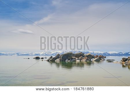 Boulders in water of the lake Tahoe, mountains covered by snow at background