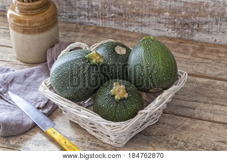 Round zucchini in a basket on a wooden table.