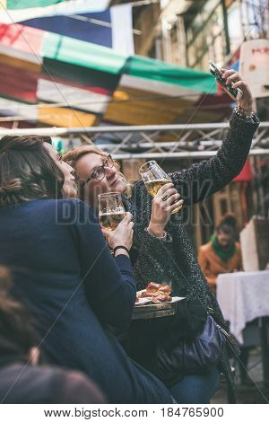 BUDAPEST, HUNGARY - MARCH 26, 2017: Unknown women tourists drinking beer and making selfie with mobile phone at Szimpla Sunday farmers' market at Szimpla Kert ruin pub in Jewish quarter of Budapest