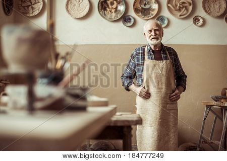 Front View Of Senior Potter In Apron Standing At Workshop