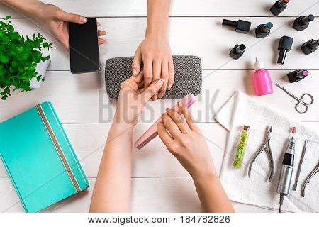 Manicure for the client. Close-up of the hands of a manicurist and client on a wooden background. Nail care. Manicure set and nail polish.