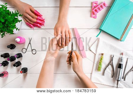 Manicure for the client. Close-up of the hands of a manicurist and client on a wooden background. Nail care. Manicure set and nail polish.