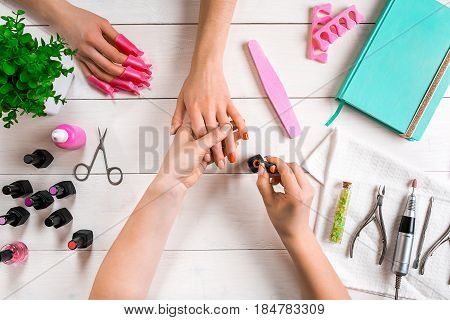 Manicure for the client. Close-up of the hands of a manicurist and client on a wooden background. Nail care. Manicure set and nail polish.