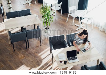 Shot of a middle aged woman making call and working on laptop while sitting at cafe.