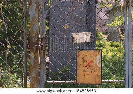 Abandoned place. Danger. Fence from the grid overgrown with branches. There is a lock on the door.