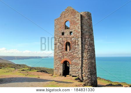 Derelict abandoned Cornish tin mine building on coast path with sea and blue sky in distance