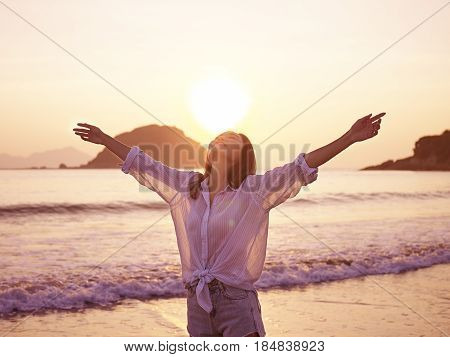 young asian woman enjoying the early morning sunlight with open arms on beach.