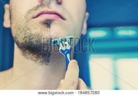 Young man shaves his short beard shaving machine tool. Half face with a beard half shaved.