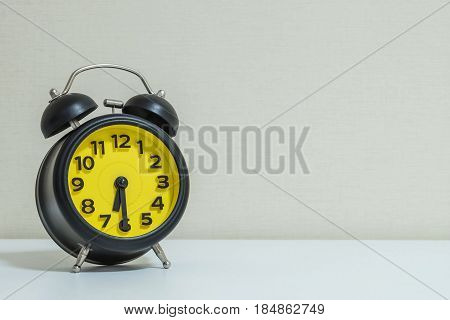 Closeup yellow and black alarm clock for decorate show half past six or 6:30 a.m. on white wood desk and cream wallpaper textured background tone with copy space