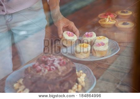 Midsection of woman holding cupcake while standing at table in cafe shop