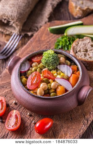 Wegetable salad in home crafted bowl with tomatoes on wooden table.