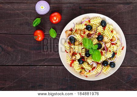 Pasta salad radiatori with chicken black olives blue onion sweet pepper on a dark wooden background. The top view.
