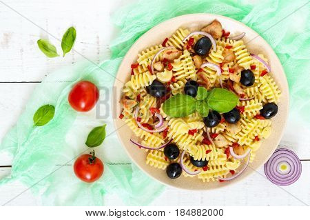 Pasta salad radiatori with chicken black olives blue onion sweet pepper on a white wooden background. The top view.