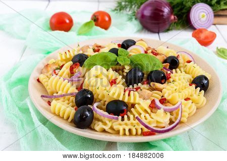 Pasta salad radiatori with chicken black olives blue onion sweet pepper on a white wooden background.