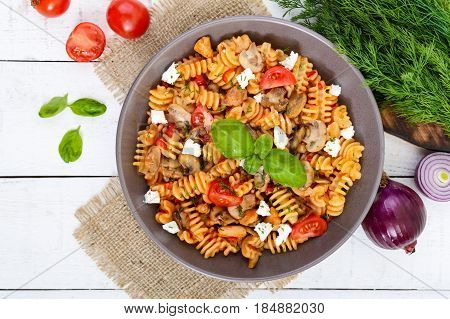 Pasta Radiatori with chicken mushrooms cherry tomatoes feta cheese and tomato sauce on a white wooden background. Top view.