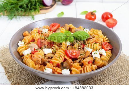 Pasta Radiatori with chicken mushrooms cherry tomatoes feta cheese and tomato sauce on a white wooden background.