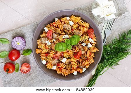 Pasta Radiatori with chicken mushrooms cherry tomatoes feta cheese and tomato sauce on a light background. Top view.