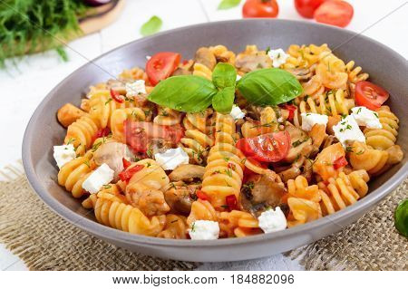 Pasta Radiatori with chicken mushrooms cherry tomatoes feta cheese and tomato sauce on a white wooden background.