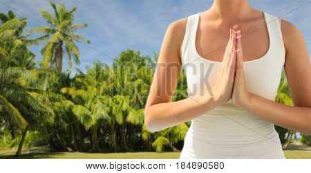 yoga and people concept - close up of woman doing namaste gesture outdoors over exotic natural background with palm trees