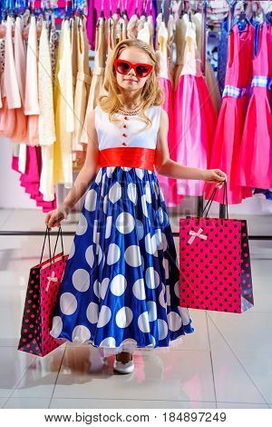 Little fashion-monger girl wearing beautiful pin-up dress and sunglasses goes shopping. Children's fashion. Sale and shopping concept. 