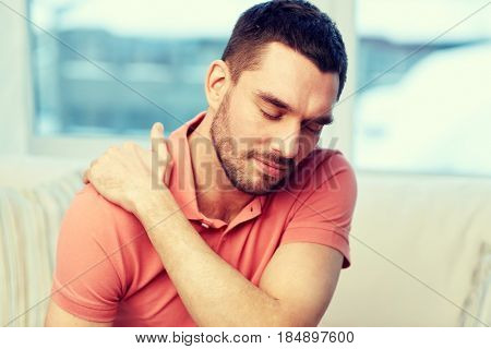 people, healthcare and problem concept - unhappy man suffering from neck or shoulder pain at home